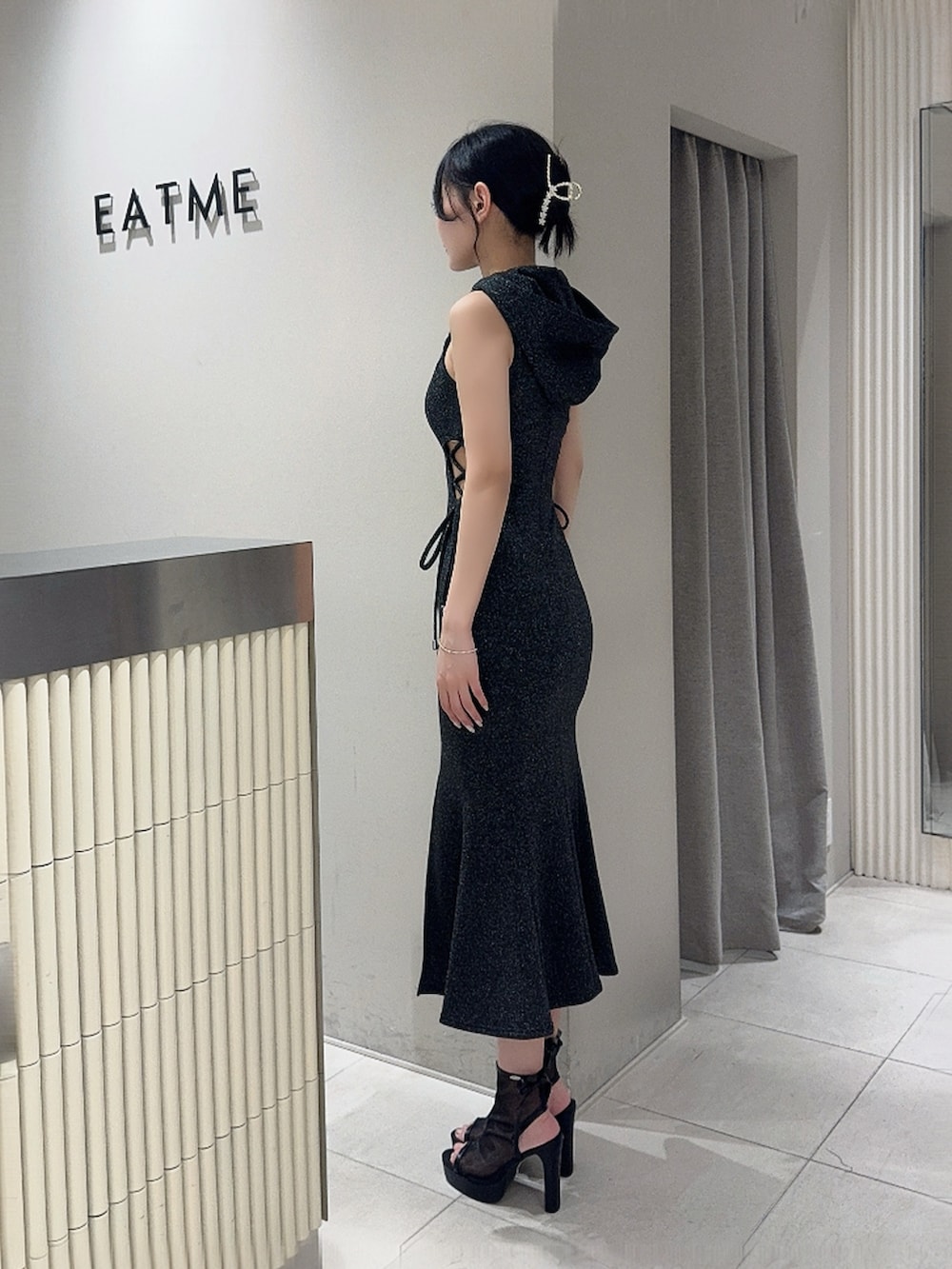 ブラック系のワンピース、ブラック系のサンダル、ピンク系のブレスレットを着用したレディースの夏コーディネートの2枚目の写真