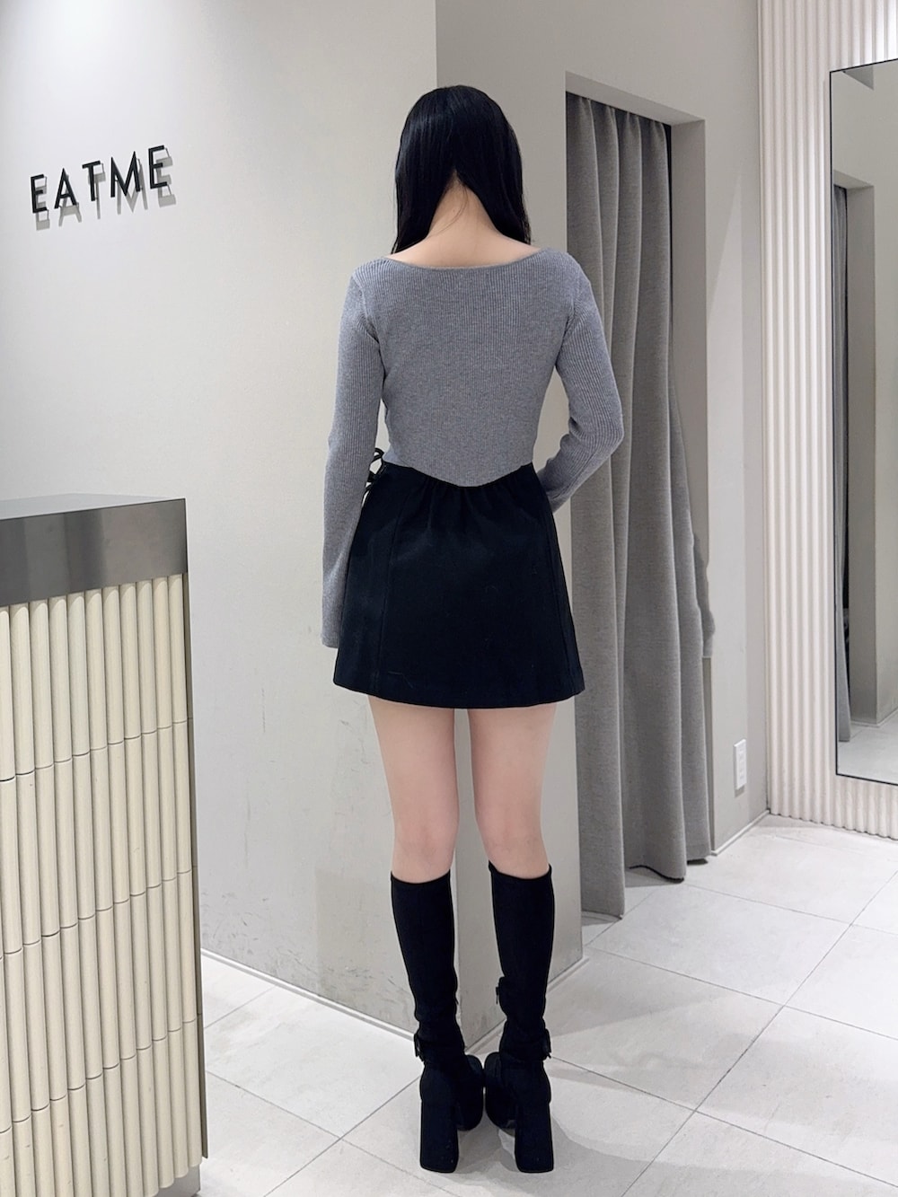 グレー系のニット/セーター、ブラック系のスカート、ブラック系のブーツを着用したレディースの秋コーディネートの3枚目の写真