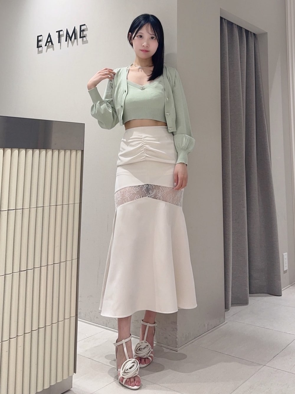 グリーン系のニット/セーター、ホワイト系のサンダル、グレー系のスカートを着用したレディースの夏コーディネートの2枚目の写真