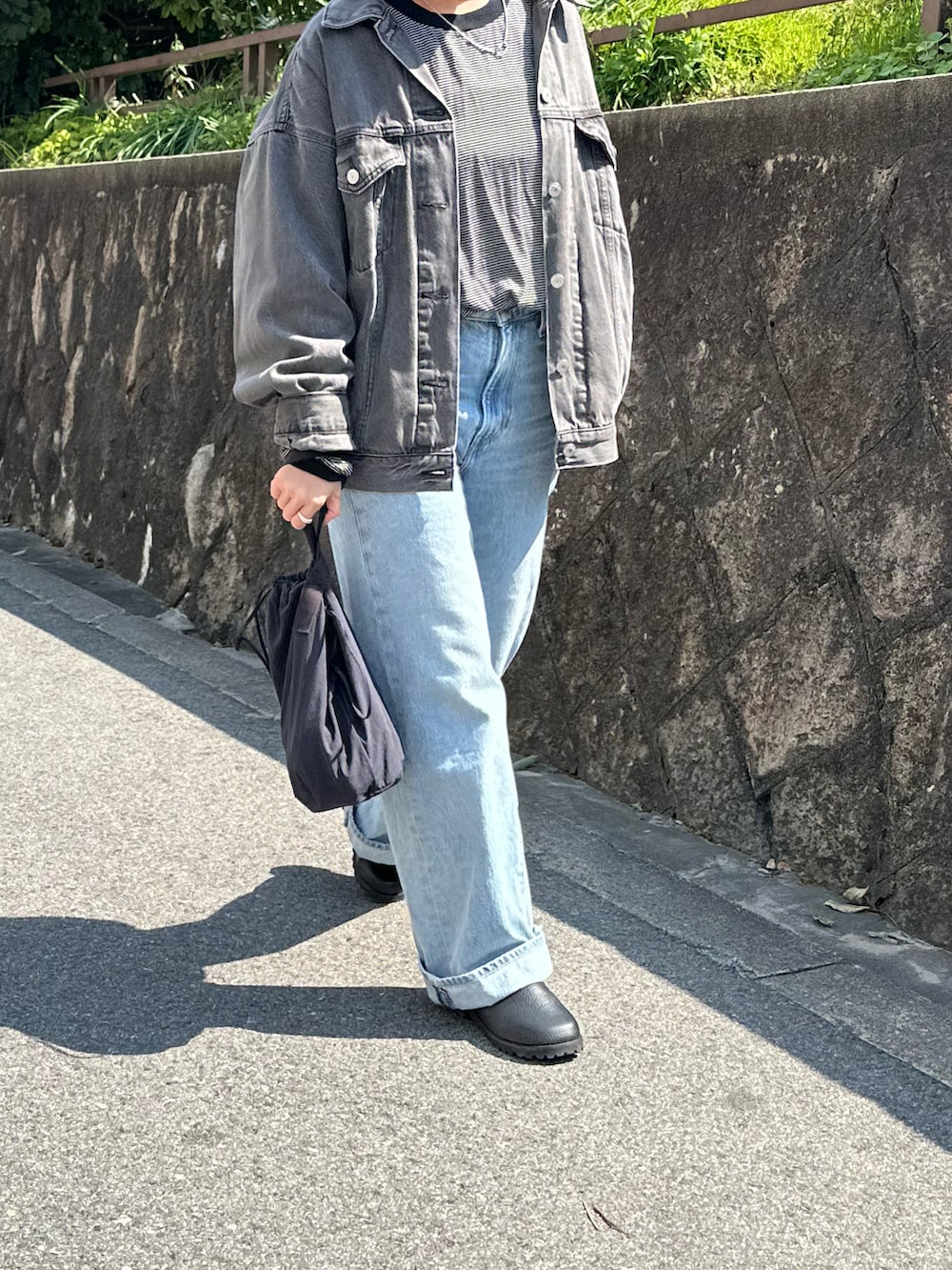 ブラック系のデニムジャケット、ブルー系のデニムパンツ、ブルー系のハンドバッグを着用したレディースの春コーディネートの2枚目の写真