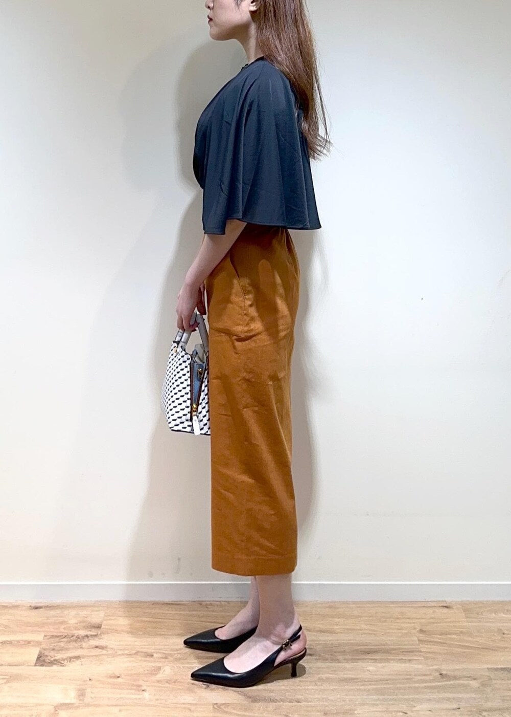 オレンジ系のスカート、ホワイト系のショルダーバッグ、ブラック系のパンプスを着用したレディースの夏コーディネートの3枚目の写真