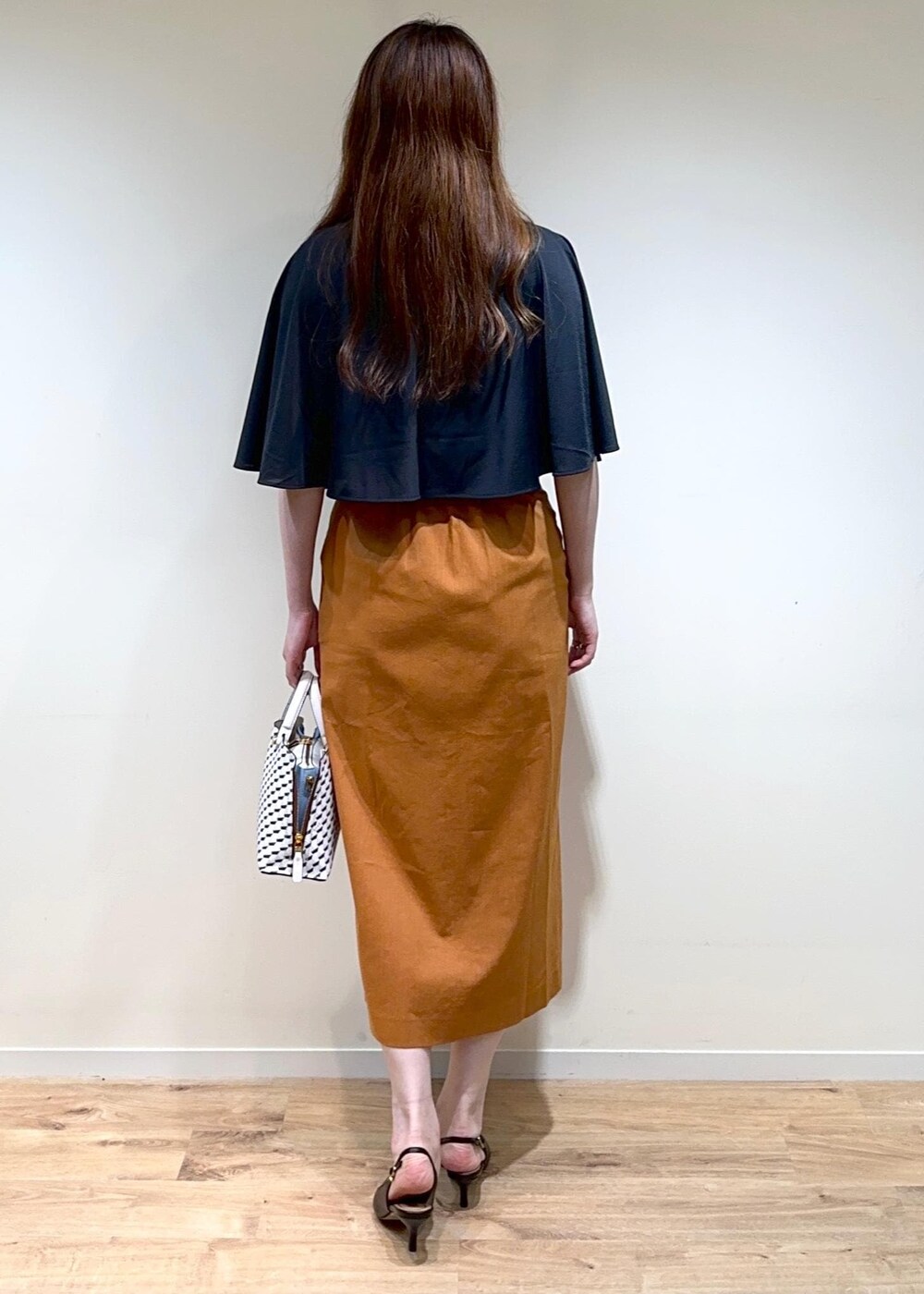 オレンジ系のスカート、ホワイト系のショルダーバッグ、ブラック系のパンプスを着用したレディースの夏コーディネートの2枚目の写真