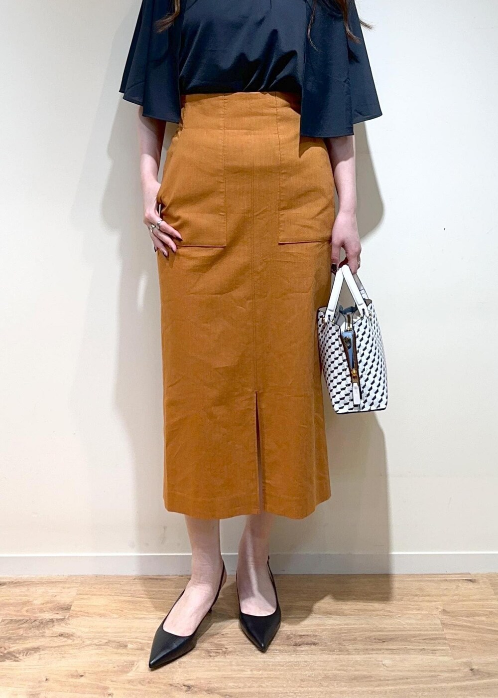 オレンジ系のスカート、ホワイト系のショルダーバッグ、ブラック系のパンプスを着用したレディースの夏コーディネートの5枚目の写真
