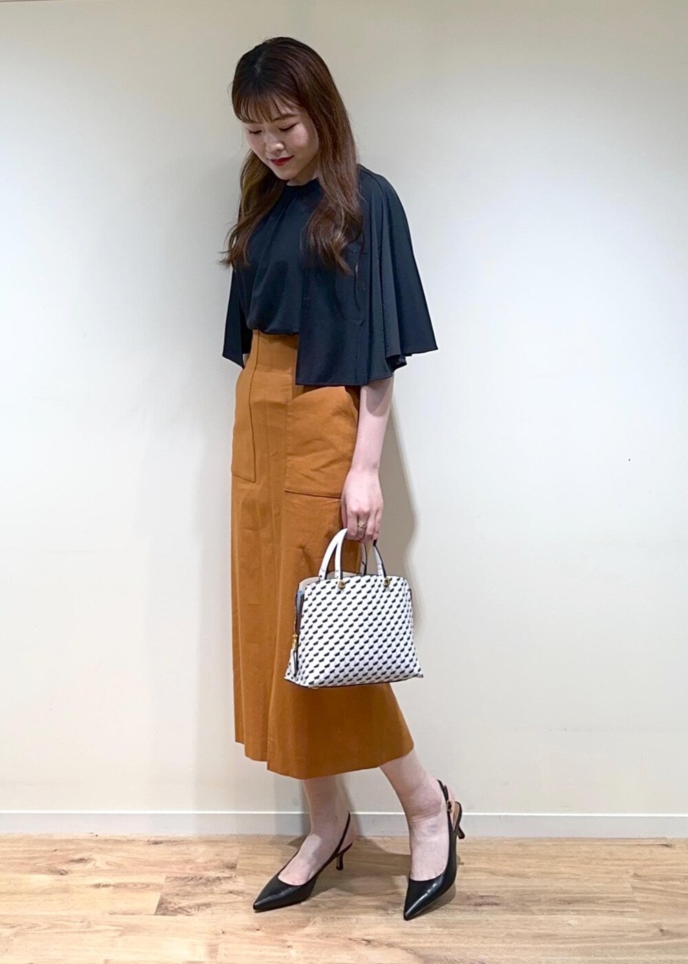 オレンジ系のスカート、ホワイト系のショルダーバッグ、ブラック系のパンプスを着用したレディースの夏コーディネートの6枚目の写真