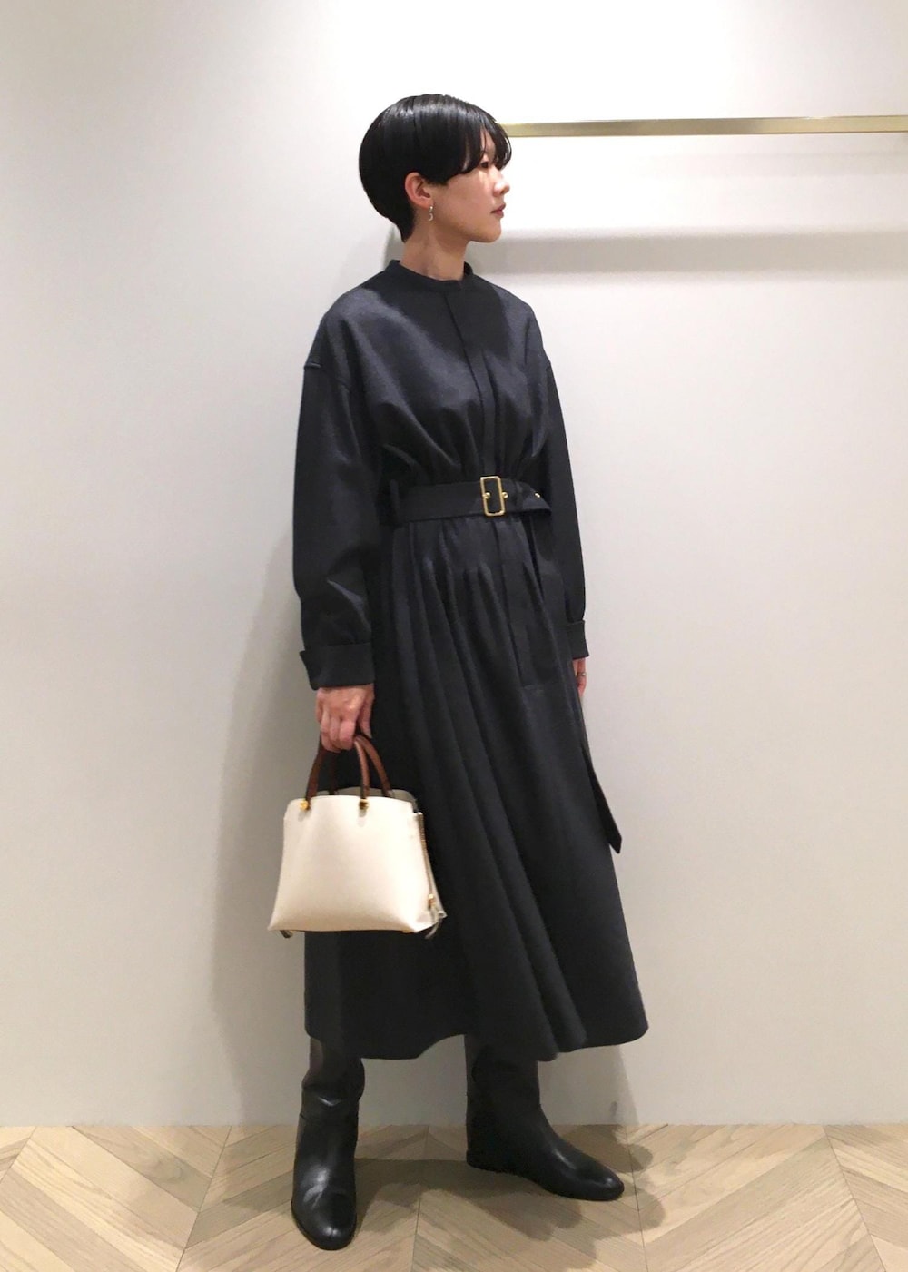 ホワイト系のハンドバッグ、ブラック系のブーツ、グレー系のワンピースを着用したレディースの冬コーディネートの2枚目の写真