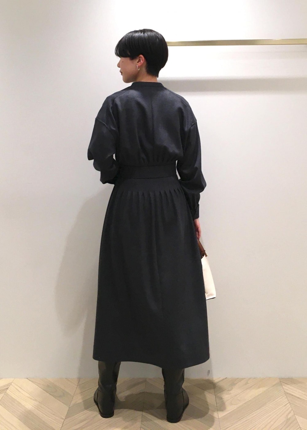 ホワイト系のハンドバッグ、ブラック系のブーツ、グレー系のワンピースを着用したレディースの冬コーディネートの3枚目の写真