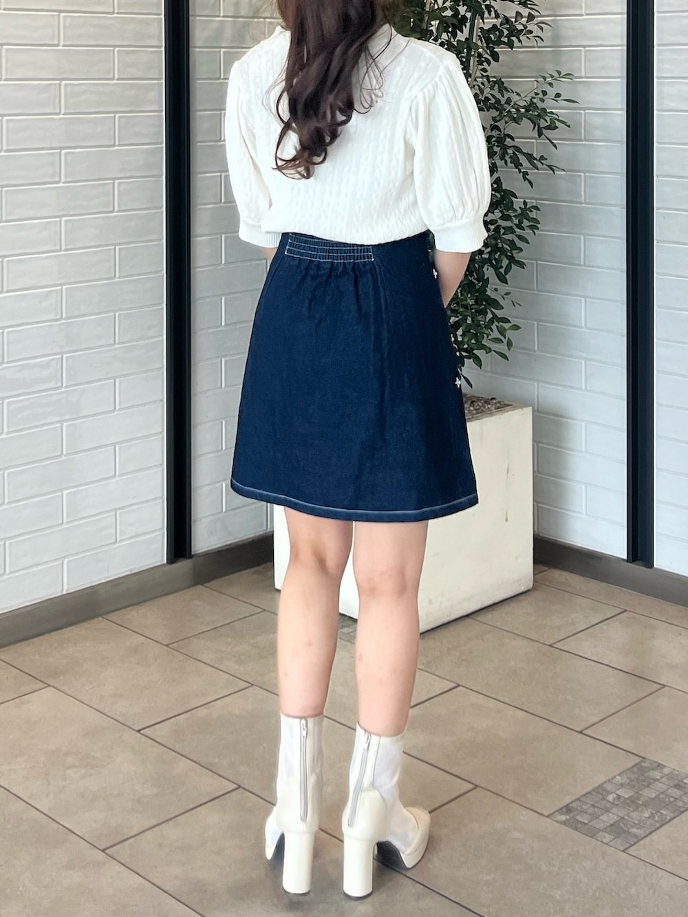 ホワイト系のニット/セーター、ブルー系のデニムスカート、ホワイト系のブーツを着用したレディースの春コーディネートの5枚目の写真