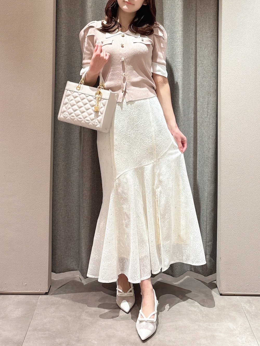 ピンク系のニット/セーター、ピンク系のハンドバッグ、ホワイト系のスカートを着用したレディースの春コーディネートの2枚目の写真