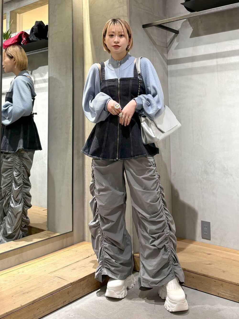 シルバー系のショルダーバッグ、ブラック系のベスト、ホワイト系のスニーカーを着用したレディースの春コーディネートの2枚目の写真