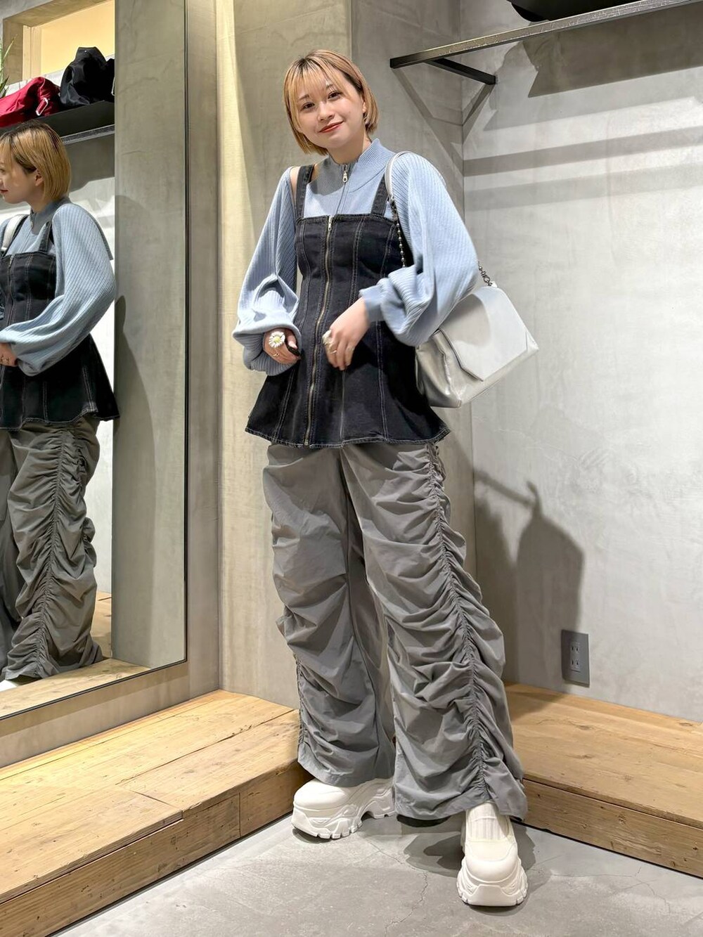 シルバー系のショルダーバッグ、ブラック系のベスト、ホワイト系のスニーカーを着用したレディースの春コーディネートの5枚目の写真