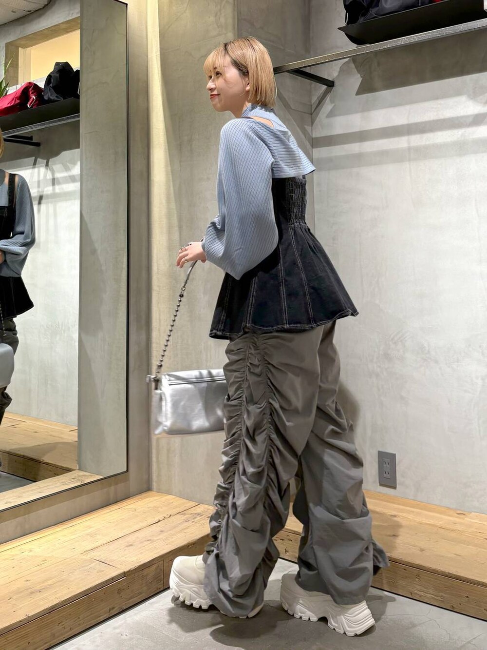 シルバー系のショルダーバッグ、ブラック系のベスト、ホワイト系のスニーカーを着用したレディースの春コーディネートの3枚目の写真