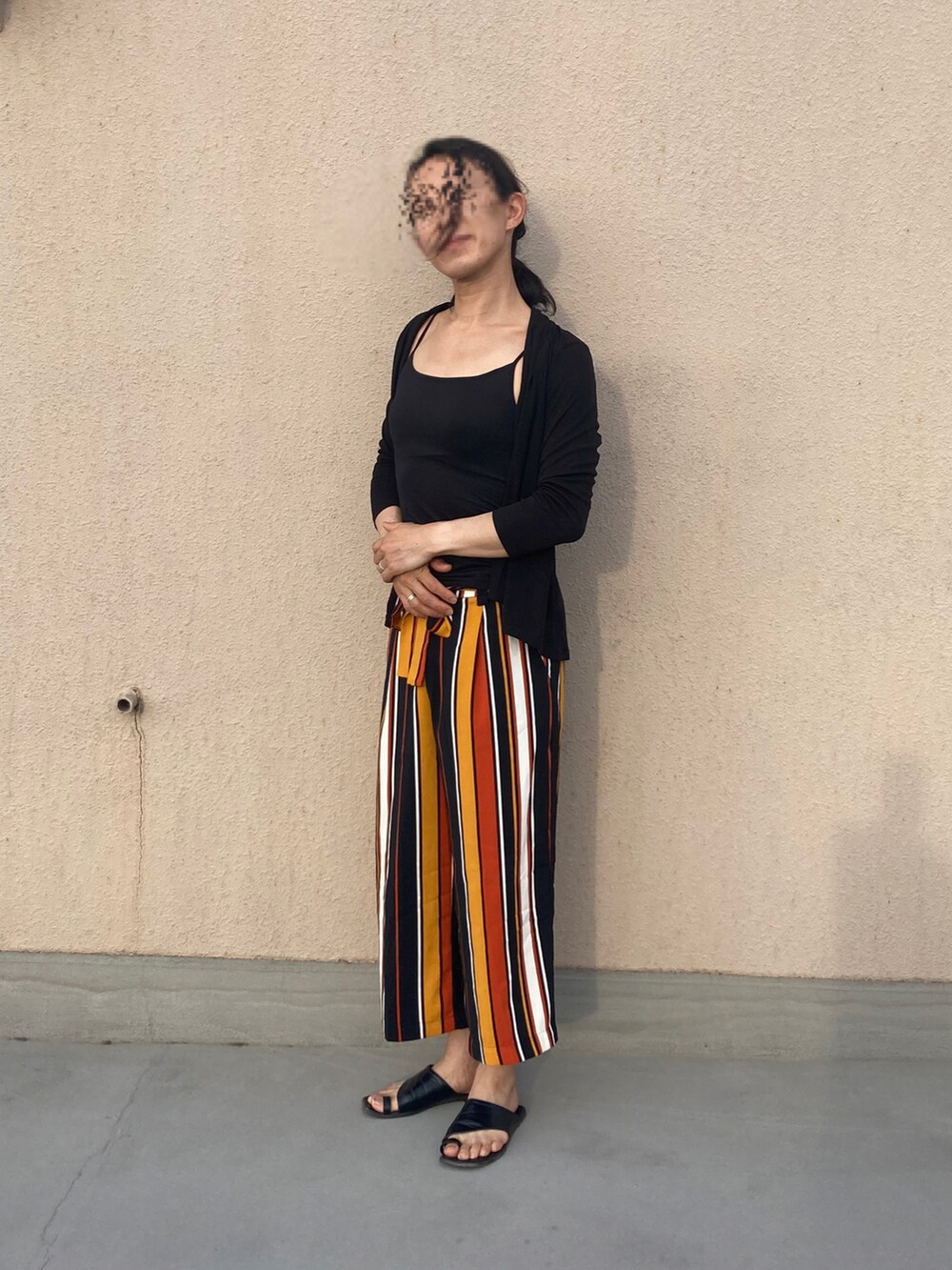 オレンジ系のパンツ、ブラック系のカーディガン/ボレロ、ブラック系のサンダルを着用したレディースの夏コーディネートの2枚目の写真