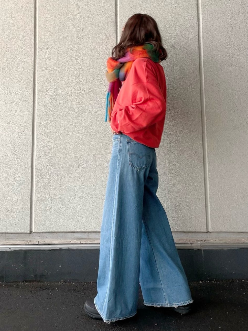 レッド系のスウェット、ブルー系のデニムパンツ、ブラック系のブーツを着用したレディースの冬コーディネートの2枚目の写真