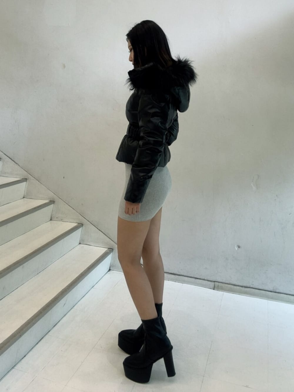 ブラック系のブーツ、ブラック系のダウンジャケット/コート、グレー系のワンピースを着用したレディースの秋コーディネートの2枚目の写真