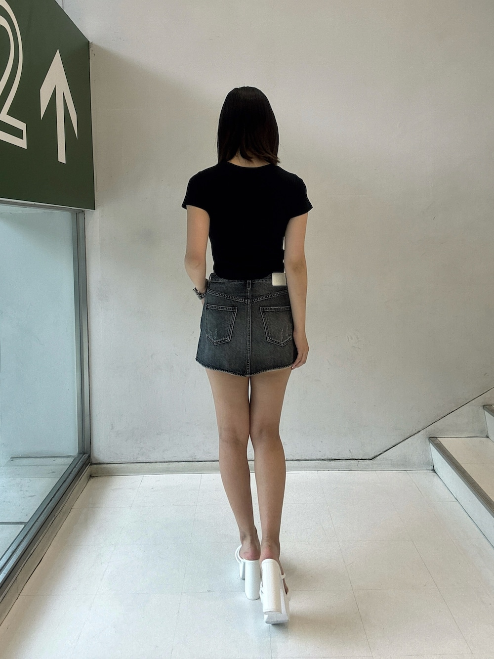 ブラック系のデニムスカート、ブラック系のTシャツ/カットソー、ホワイト系のサンダルを着用したレディースの夏コーディネートの3枚目の写真