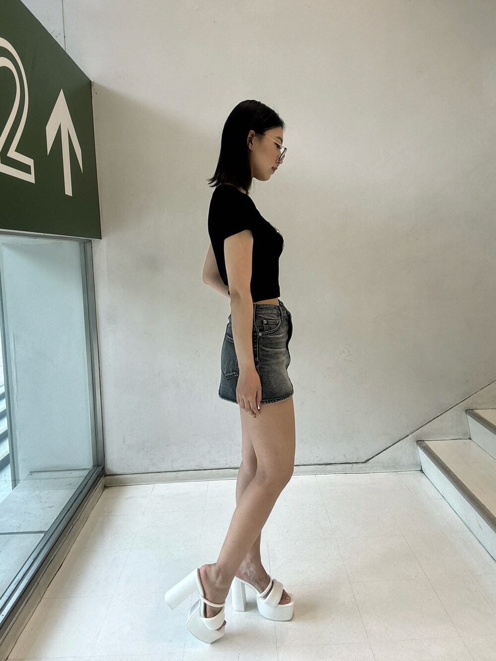ブラック系のデニムスカート、ブラック系のTシャツ/カットソー、ホワイト系のサンダルを着用したレディースの夏コーディネートの2枚目の写真