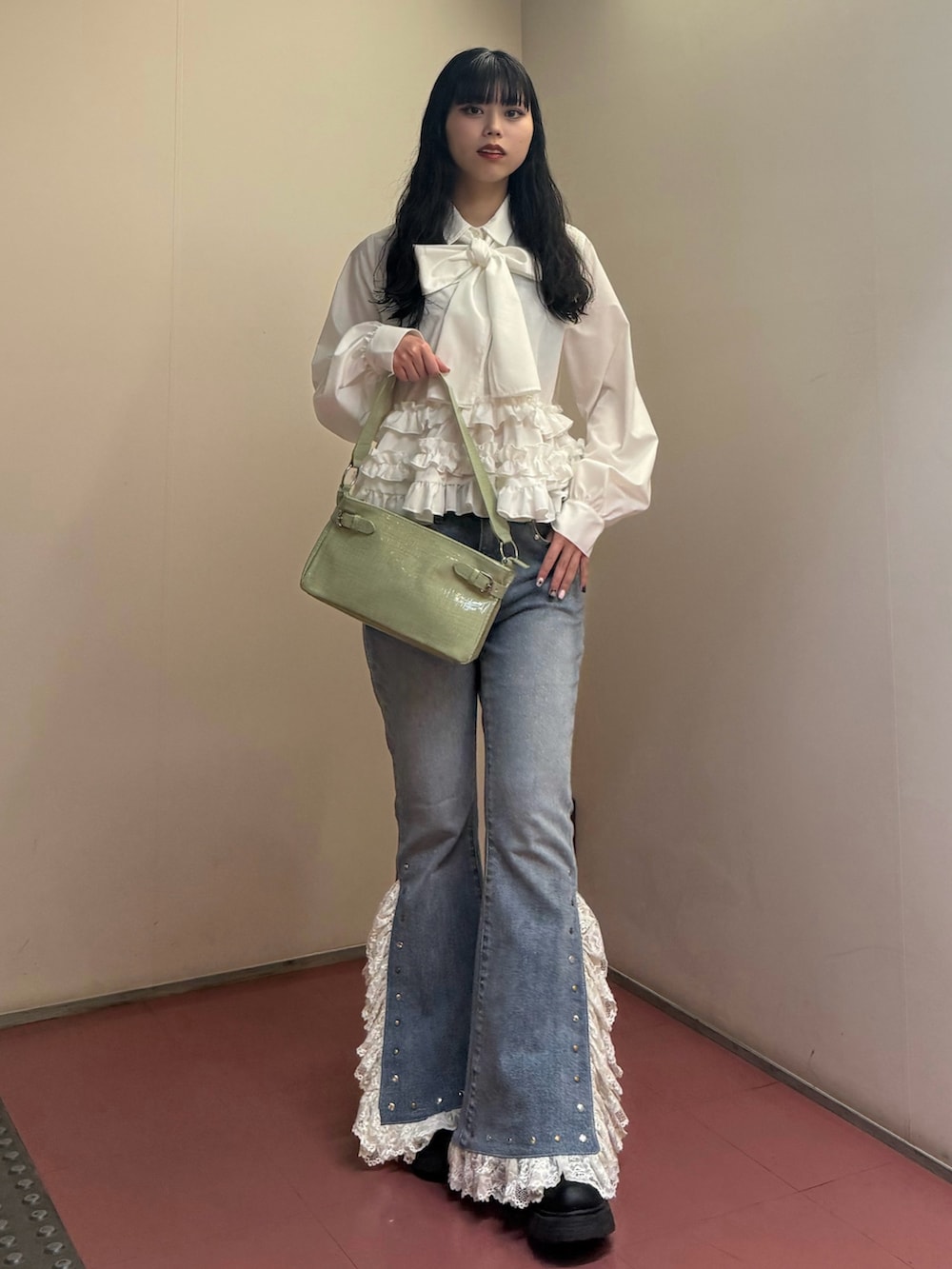 グリーン系のハンドバッグ、ホワイト系のシャツ/ブラウス、ブルー系のデニムパンツを着用したレディースの冬コーディネートの2枚目の写真