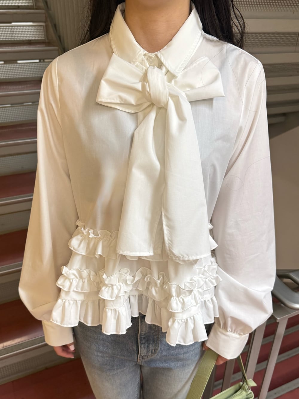 グリーン系のハンドバッグ、ホワイト系のシャツ/ブラウス、ブルー系のデニムパンツを着用したレディースの冬コーディネートの5枚目の写真