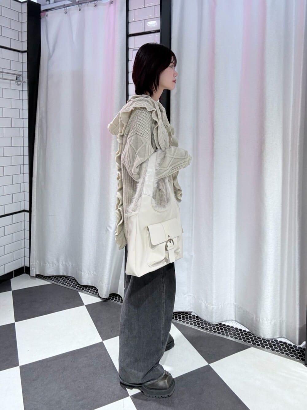 ブラック系のデニムパンツ、ホワイト系のニット/セーター、ホワイト系のハンドバッグを着用したレディースの冬コーディネートの2枚目の写真