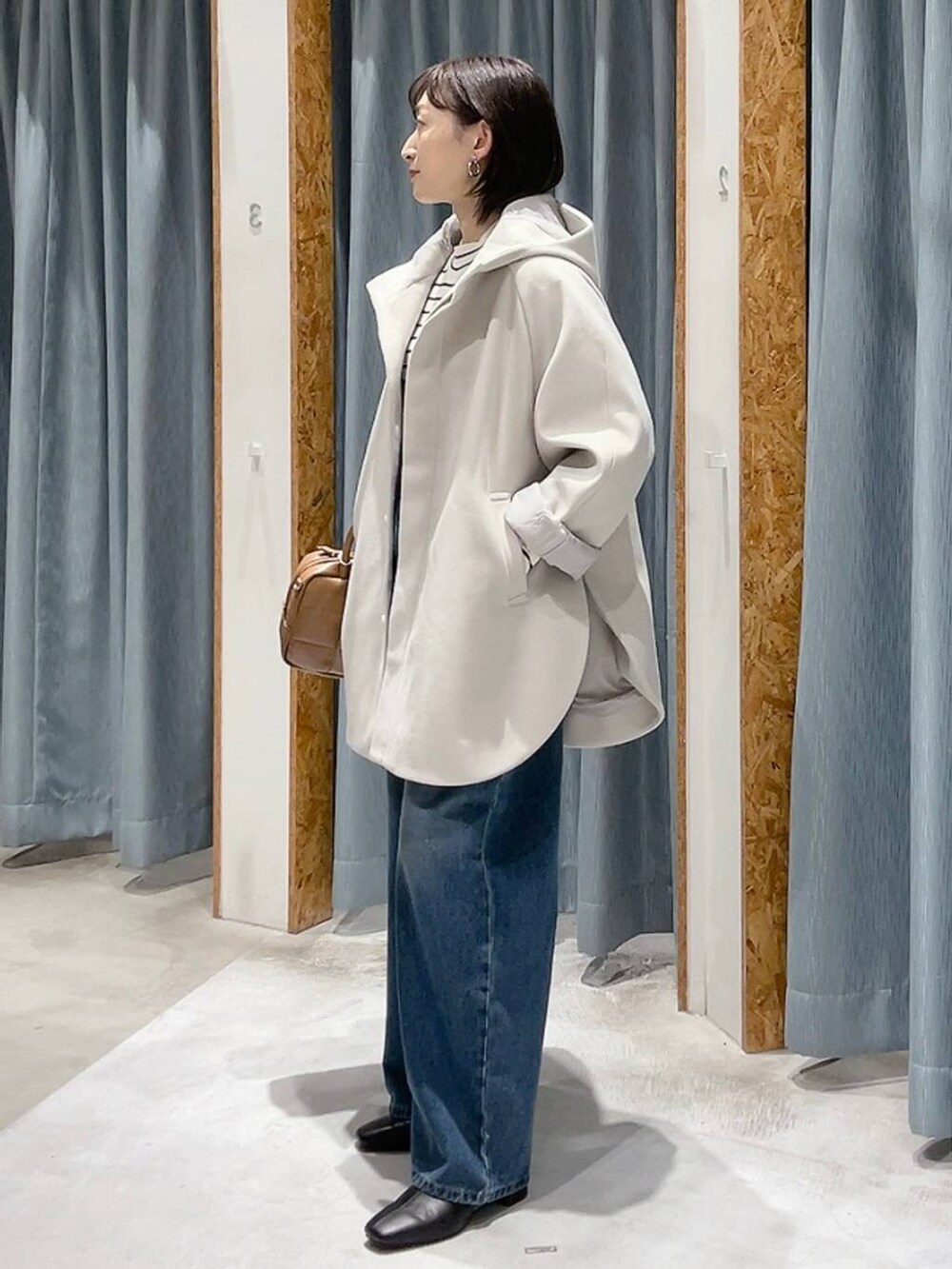 ホワイト系のポンチョ、ホワイト系のニット/セーター、ブルー系のデニムパンツを着用したレディースの秋コーディネートの6枚目の写真