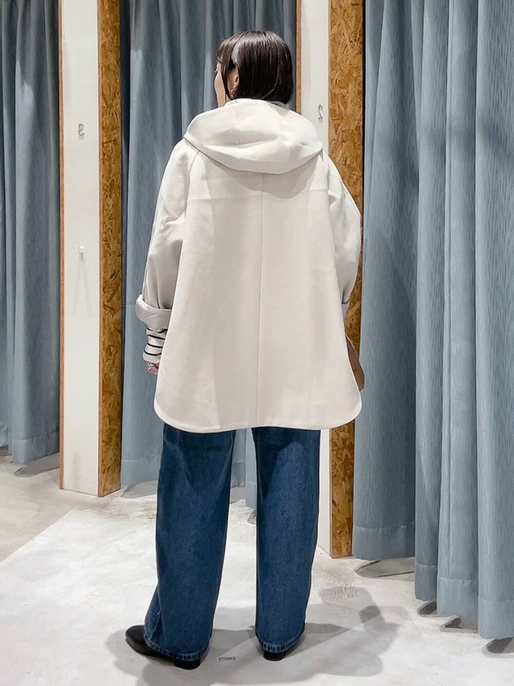 ホワイト系のポンチョ、ホワイト系のニット/セーター、ブルー系のデニムパンツを着用したレディースの秋コーディネートの5枚目の写真