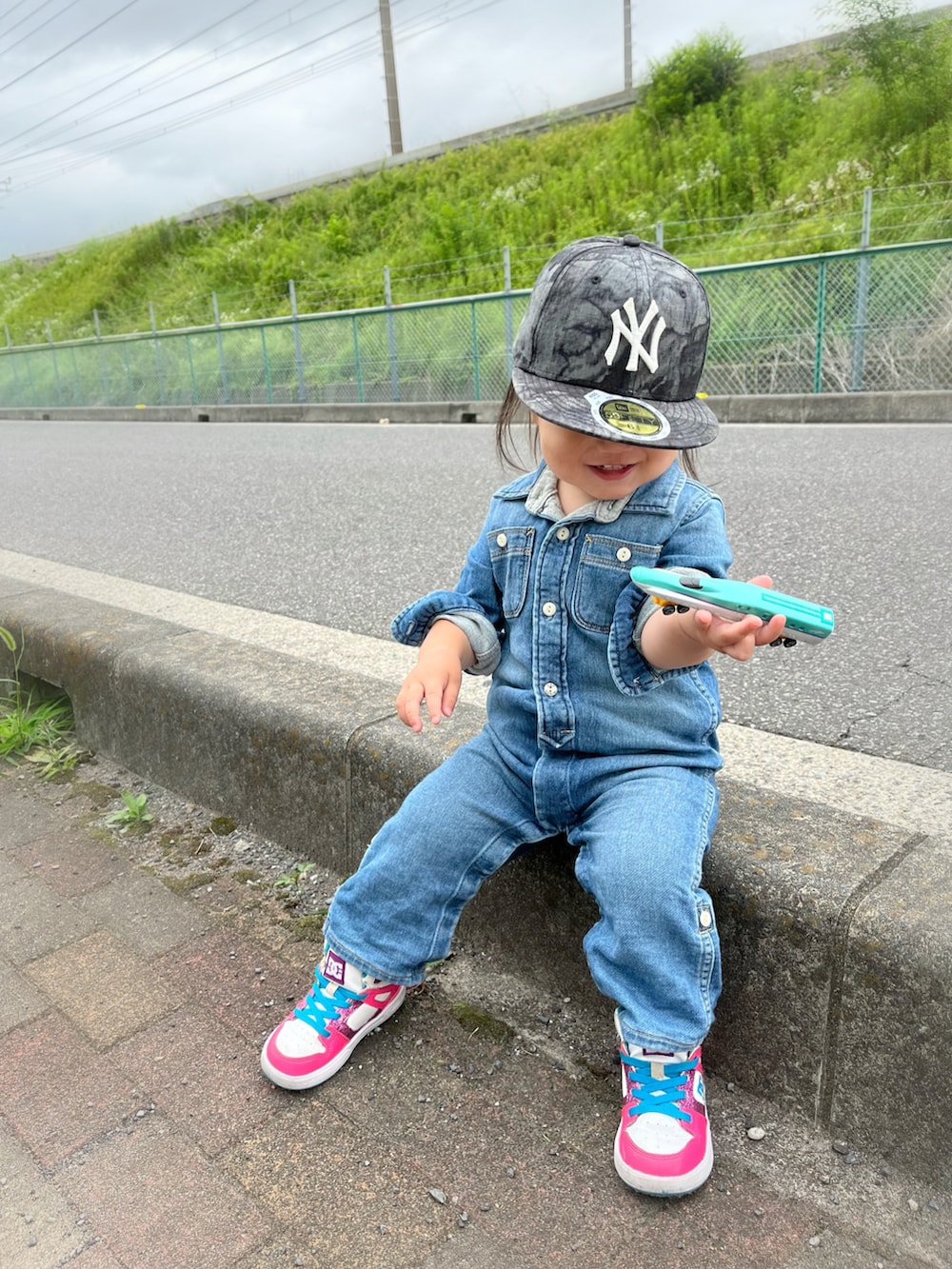 ブルー系のつなぎ/オールインワン、ピンク系のスニーカー、ブラック系のキャップを着用したキッズの夏コーディネートの3枚目の写真