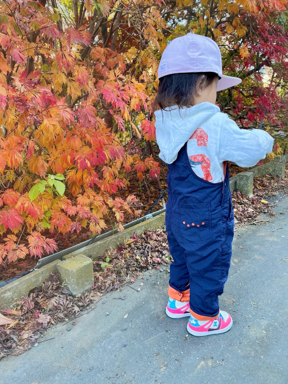 ブルー系のサロペット/オーバーオール、ピンク系のスニーカー、ピンク系のキャップを着用したキッズの秋コーディネートの3枚目の写真