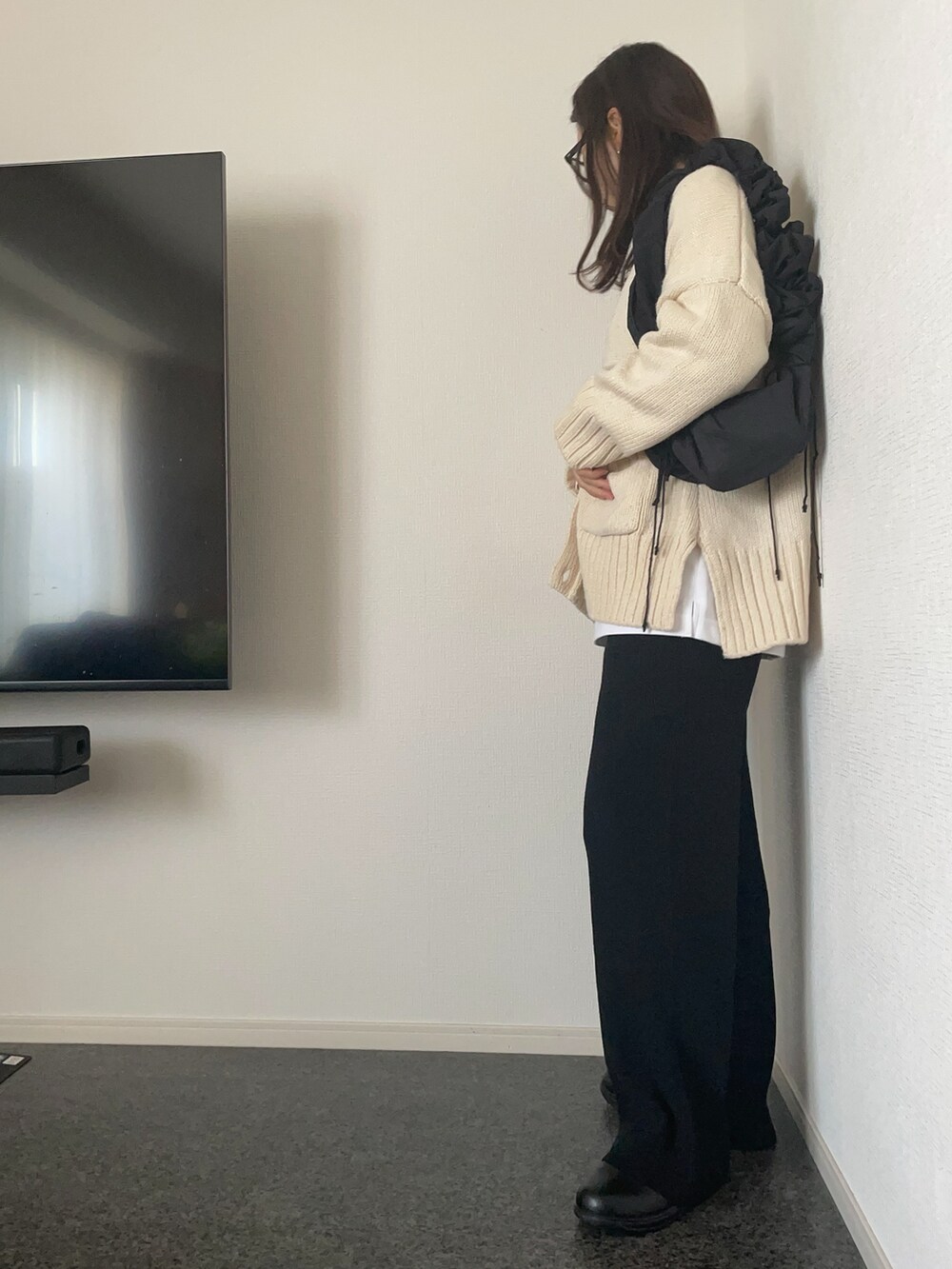 ブラック系のハンドバッグ、ホワイト系のカーディガン/ボレロ、ブラック系のパンツを着用したレディースの秋コーディネートの2枚目の写真