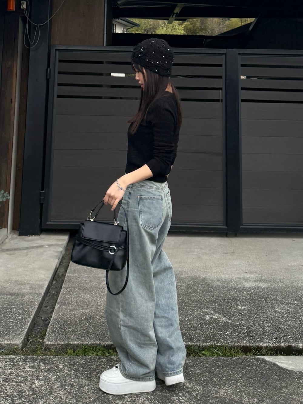 ブルー系のデニムパンツ、ブラック系のニット/セーター、ブラック系のショルダーバッグを着用したレディースの春コーディネートの2枚目の写真