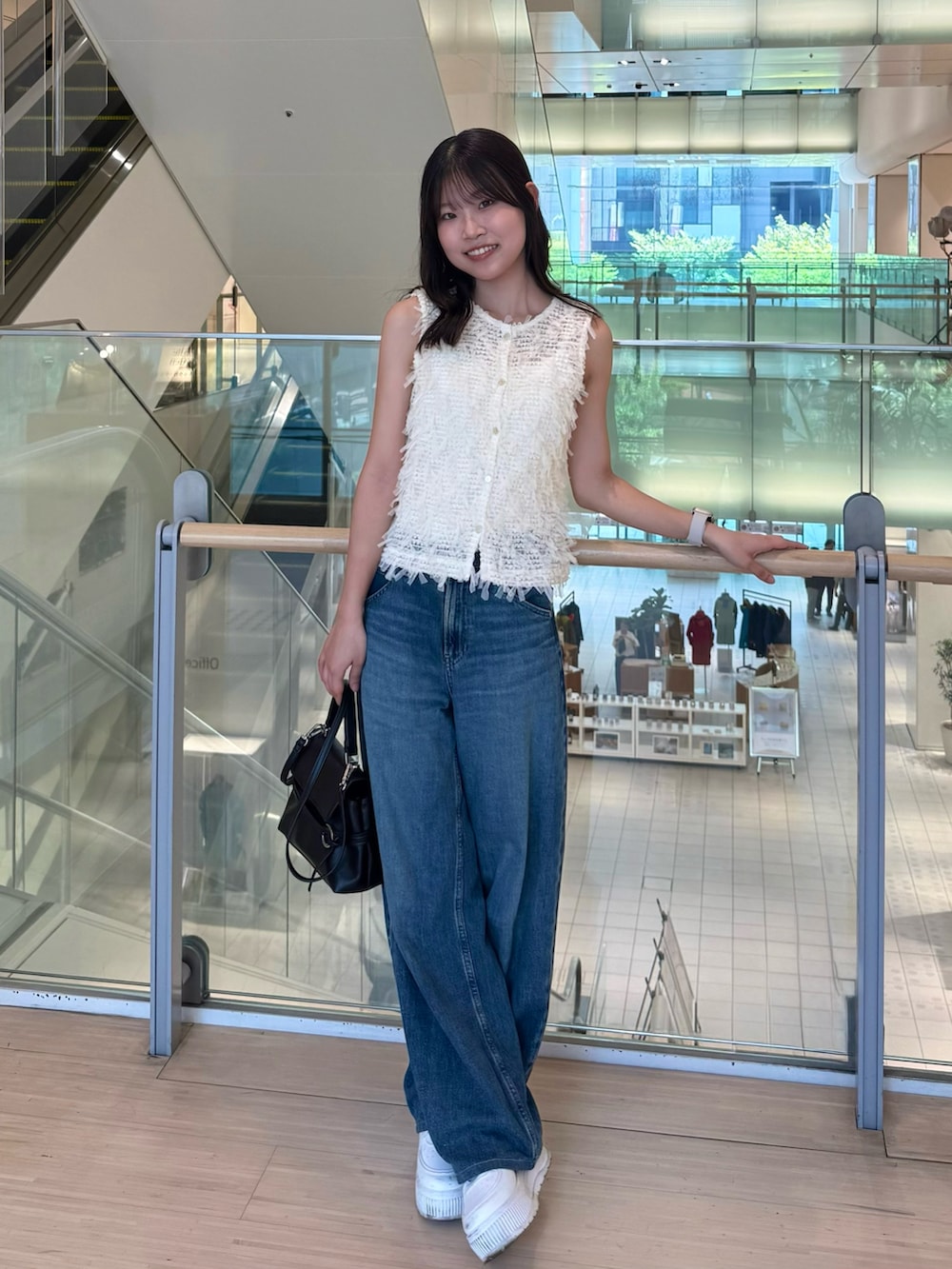 ブラック系のショルダーバッグ、ブルー系のデニムパンツ、ホワイト系のベストを着用したレディースの夏コーディネートの2枚目の写真