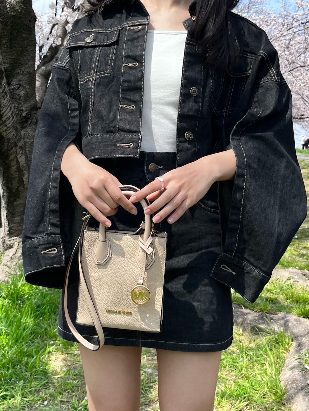 ベージュ系のショルダーバッグ、ブラック系のデニムジャケット、ブラック系のデニムスカートを着用したレディースの春コーディネートの2枚目の写真