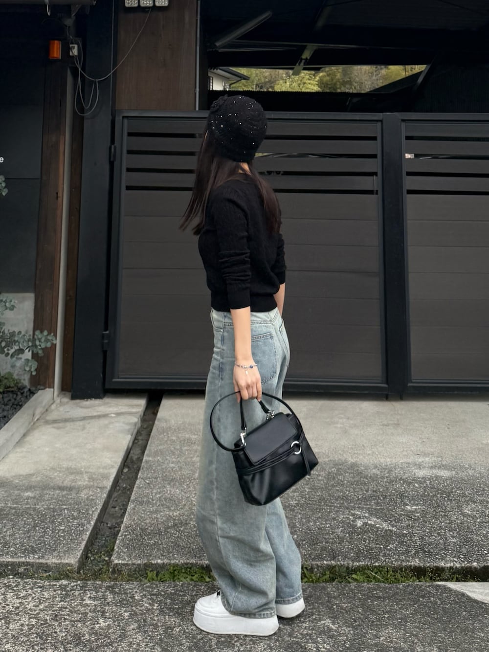 ブルー系のデニムパンツ、ブラック系のニット/セーター、ブラック系のショルダーバッグを着用したレディースの春コーディネートの3枚目の写真