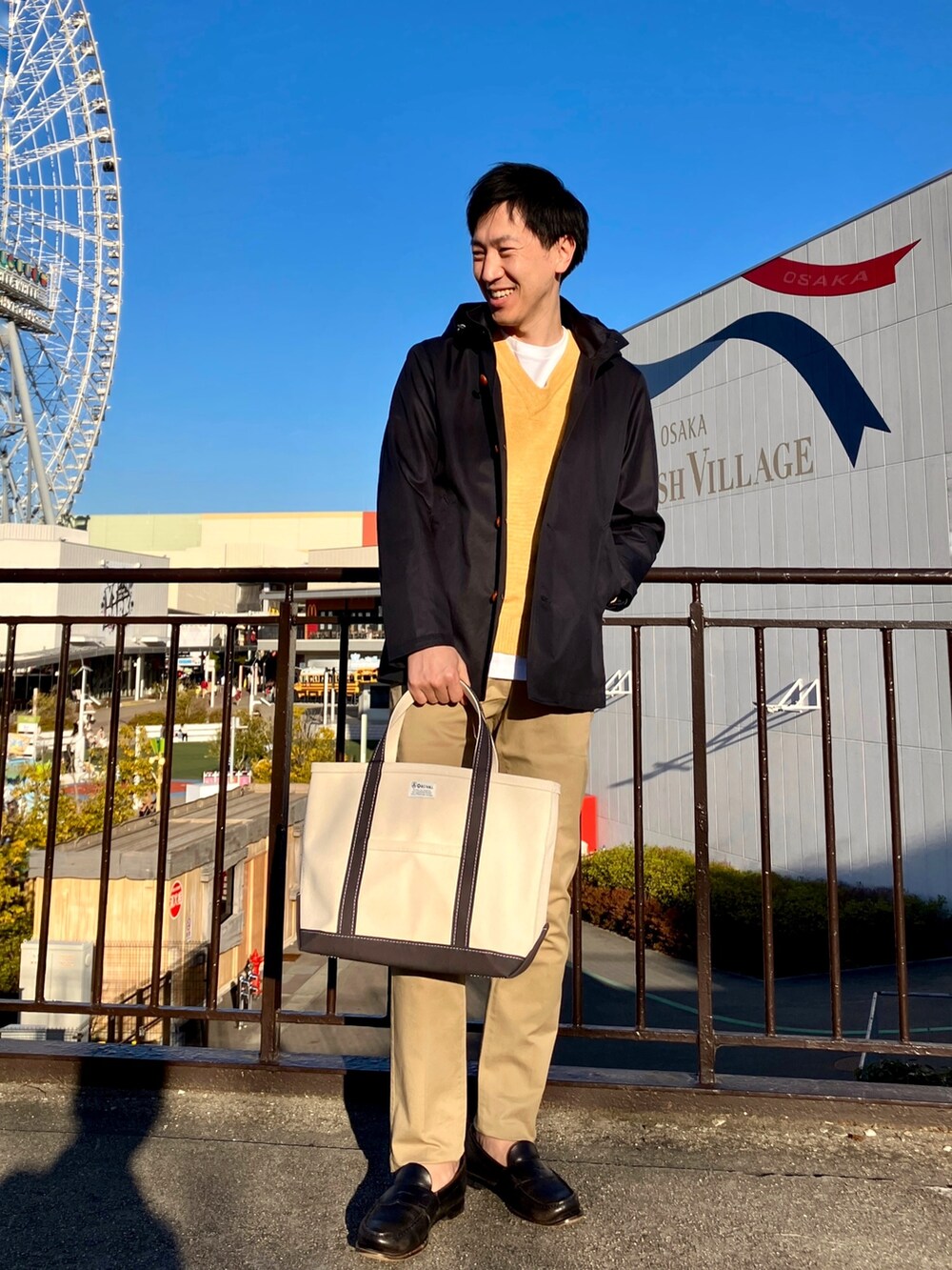 ブルー系のブルゾン、ホワイト系のトートバッグ、ベージュ系のチノパンツを着用したメンズの春コーディネートの2枚目の写真