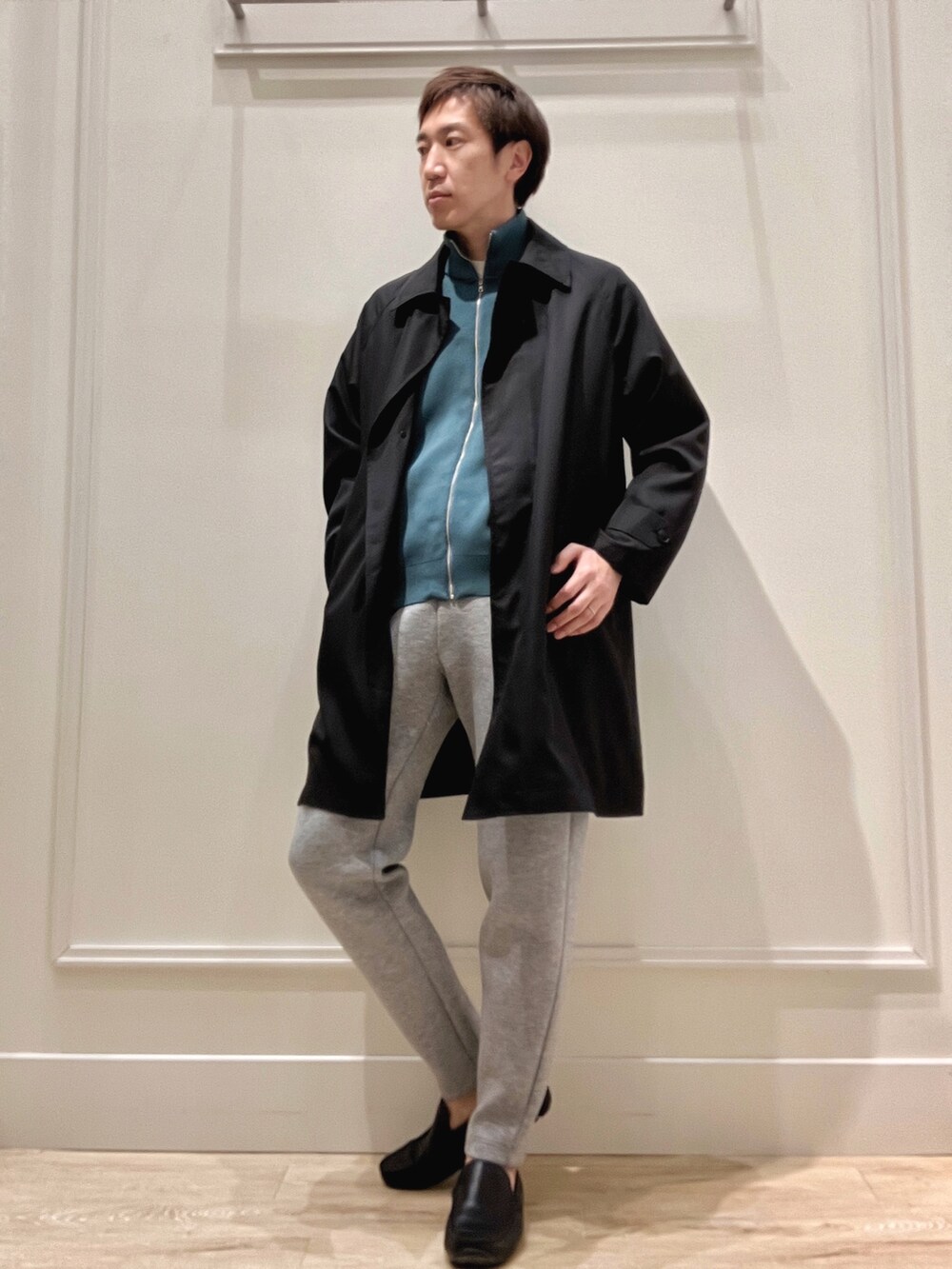 ブラック系のステンカラーコート、ブルー系のニット/セーター、グレー系のその他パンツを着用したメンズの春コーディネートの2枚目の写真