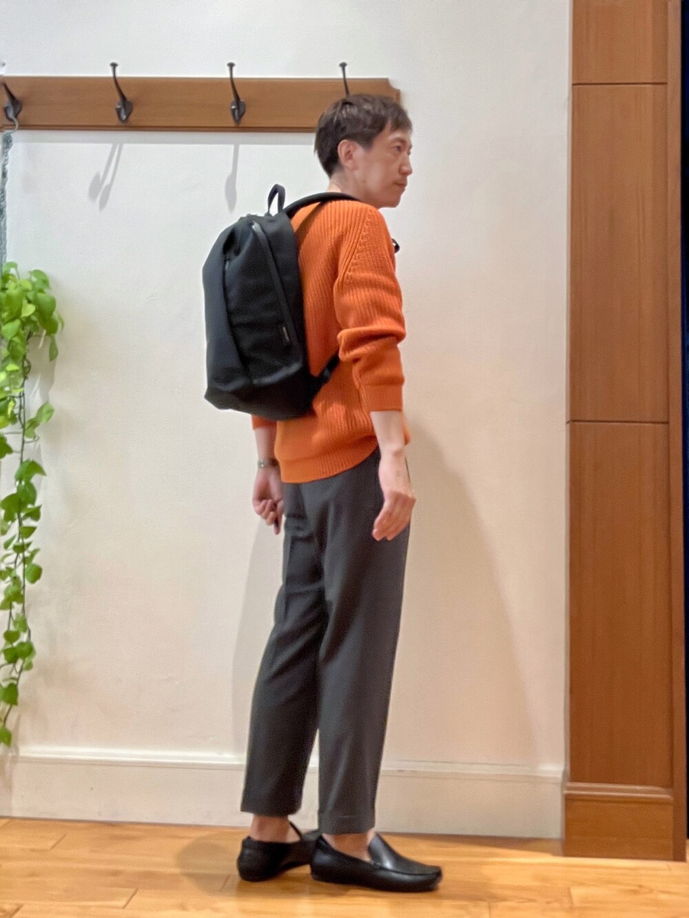 グレー系のスラックス、ブラック系のバックパック/リュック、オレンジ系のニット/セーターを着用したメンズの夏コーディネートの5枚目の写真