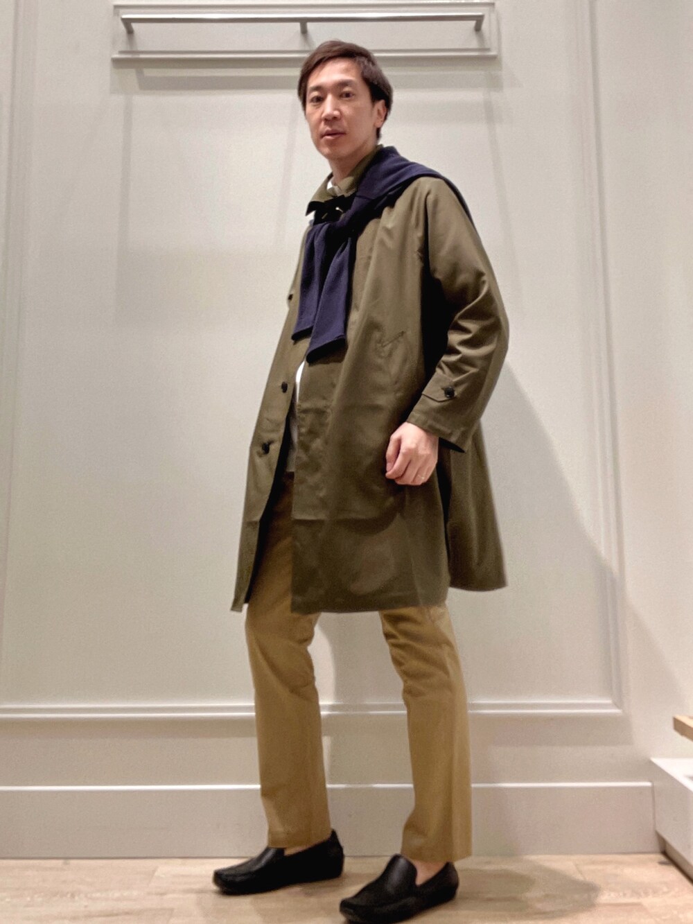 グリーン系のステンカラーコート、ベージュ系のチノパンツ、ブルー系のカーディガン/ボレロを着用したメンズの冬コーディネートの2枚目の写真