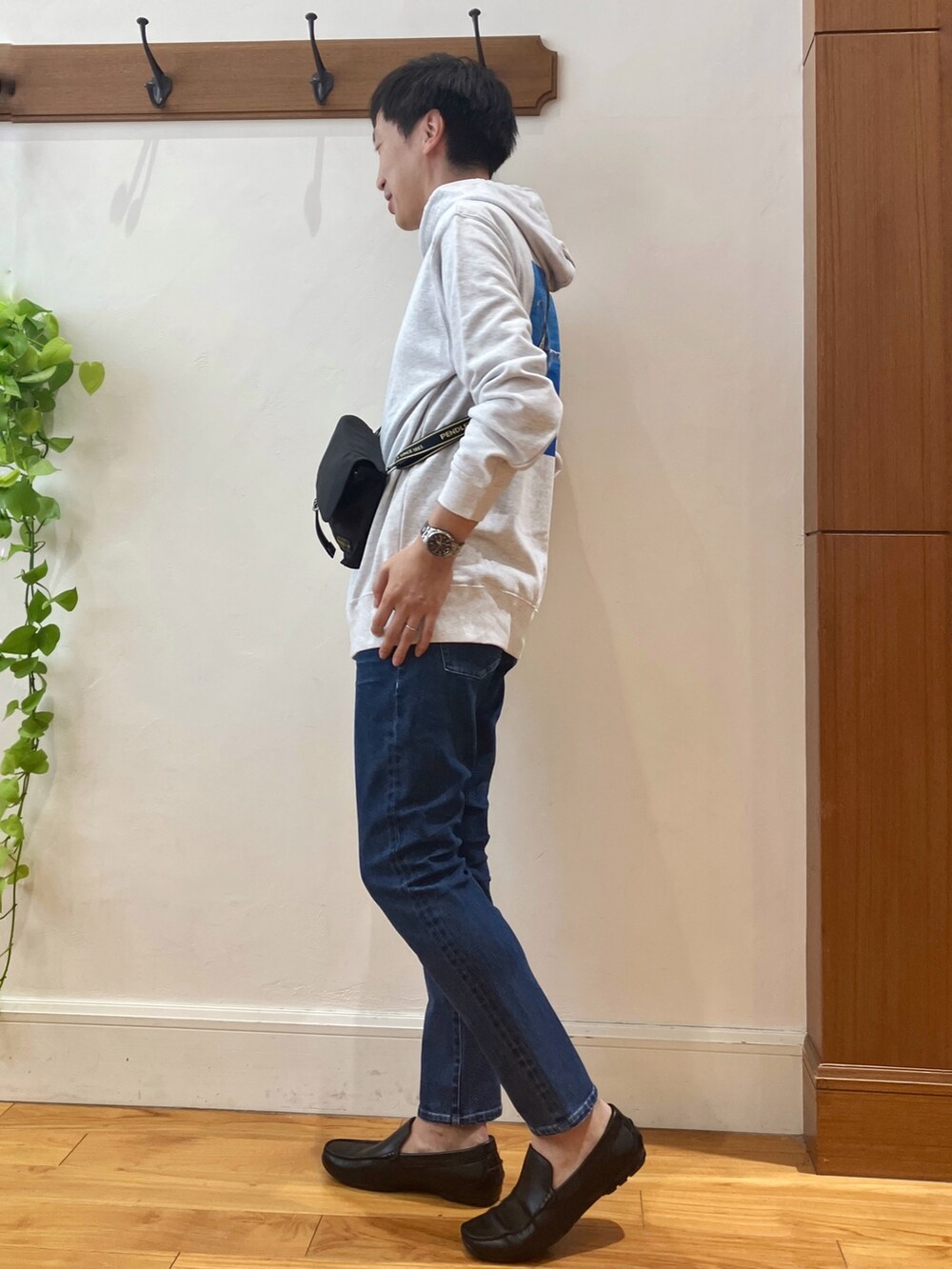 グレー系のパーカー、ブラック系のショルダーバッグ、ブルー系のデニムパンツを着用したメンズの秋コーディネートの2枚目の写真