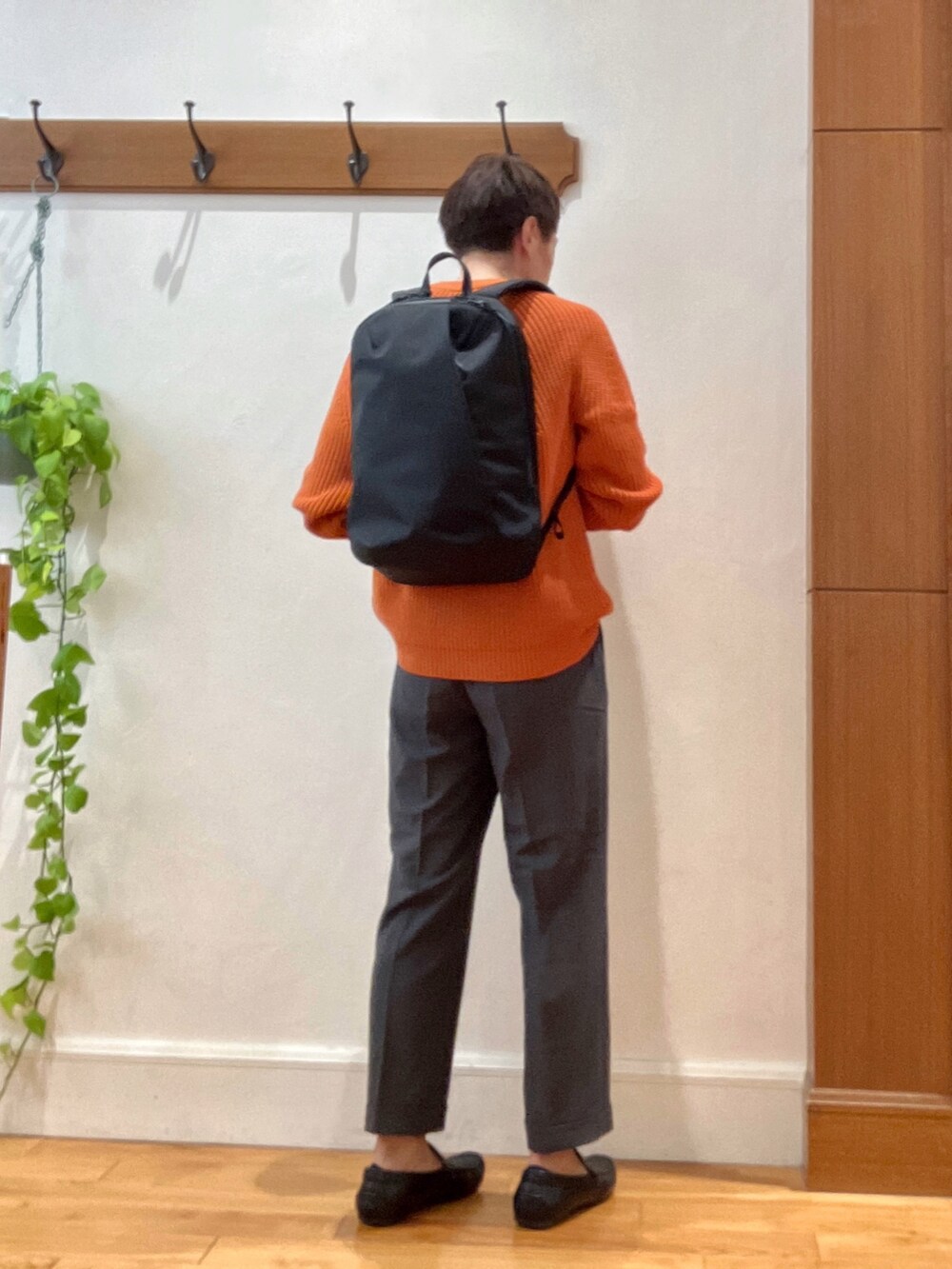 グレー系のスラックス、ブラック系のバックパック/リュック、オレンジ系のニット/セーターを着用したメンズの夏コーディネートの4枚目の写真