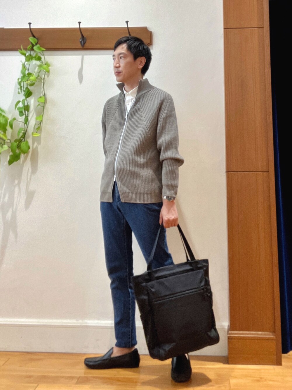 グレー系のニット/セーター、ホワイト系のシャツ/ブラウス、ブルー系のデニムパンツを着用したメンズの秋コーディネートの2枚目の写真