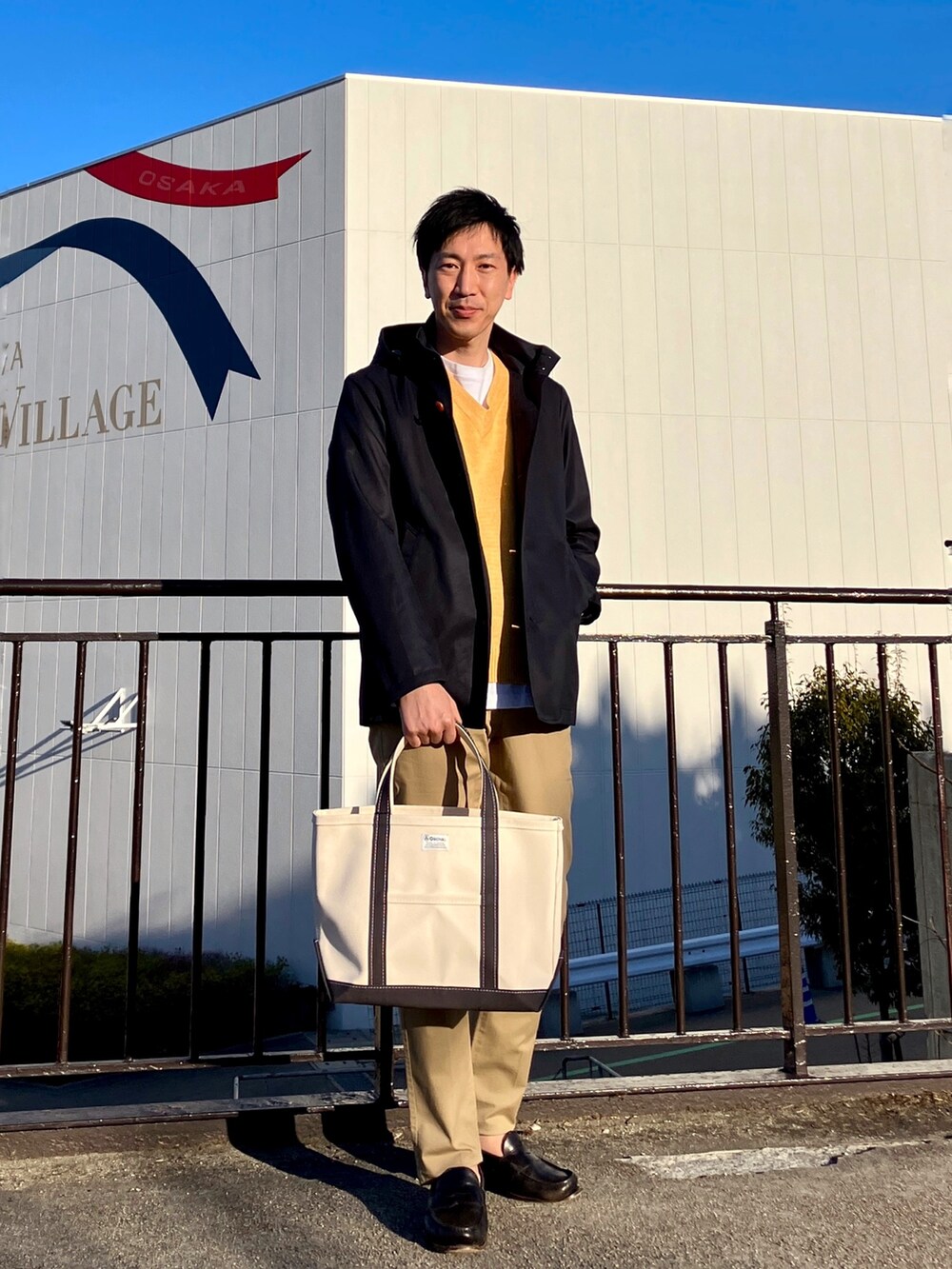 ブルー系のブルゾン、ホワイト系のトートバッグ、ベージュ系のチノパンツを着用したメンズの春コーディネートの3枚目の写真