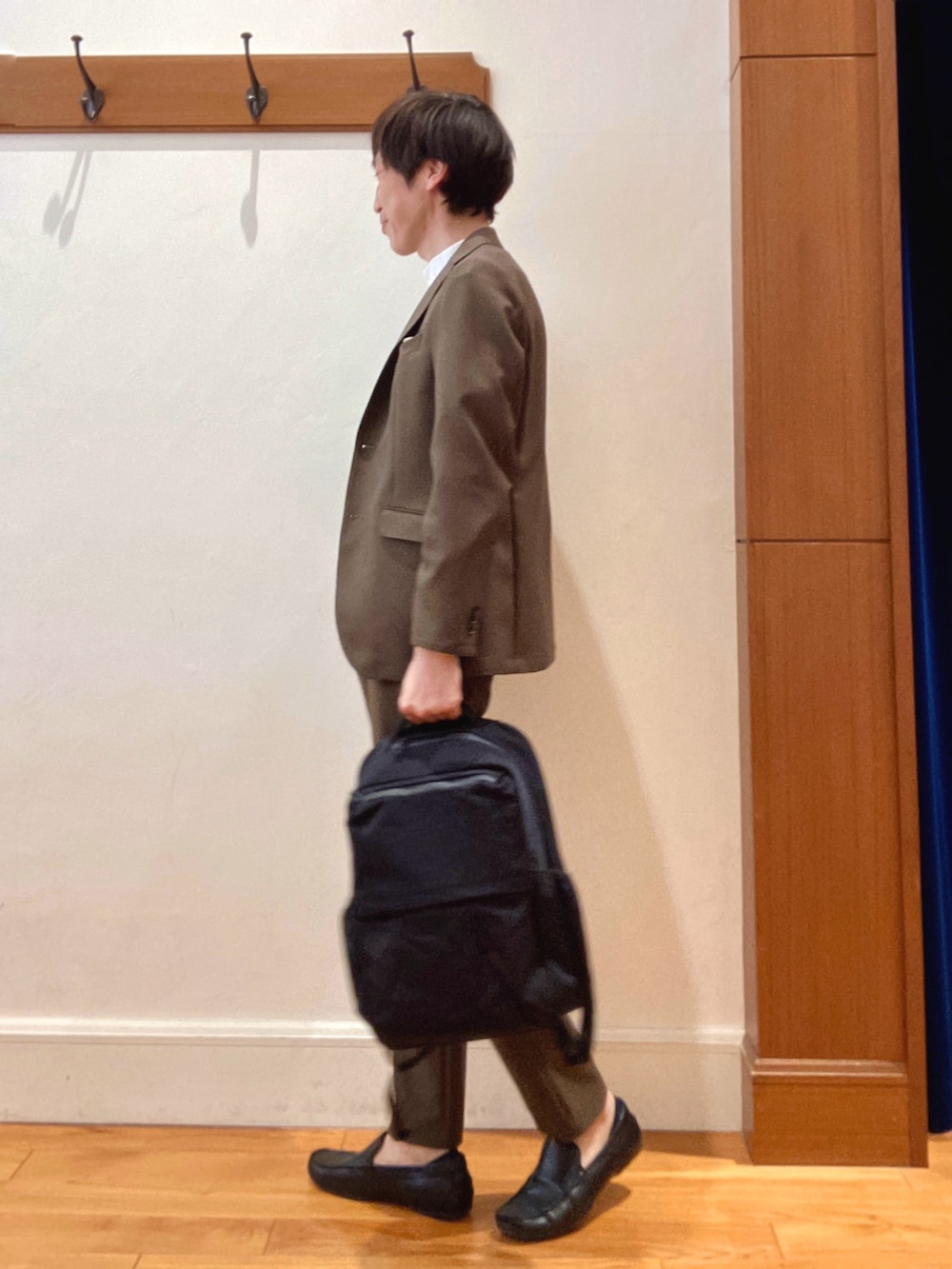 ブラウン系のテーラードジャケット、ブラック系のバックパック/リュック、ブラウン系のその他パンツを着用したメンズの春コーディネートの2枚目の写真