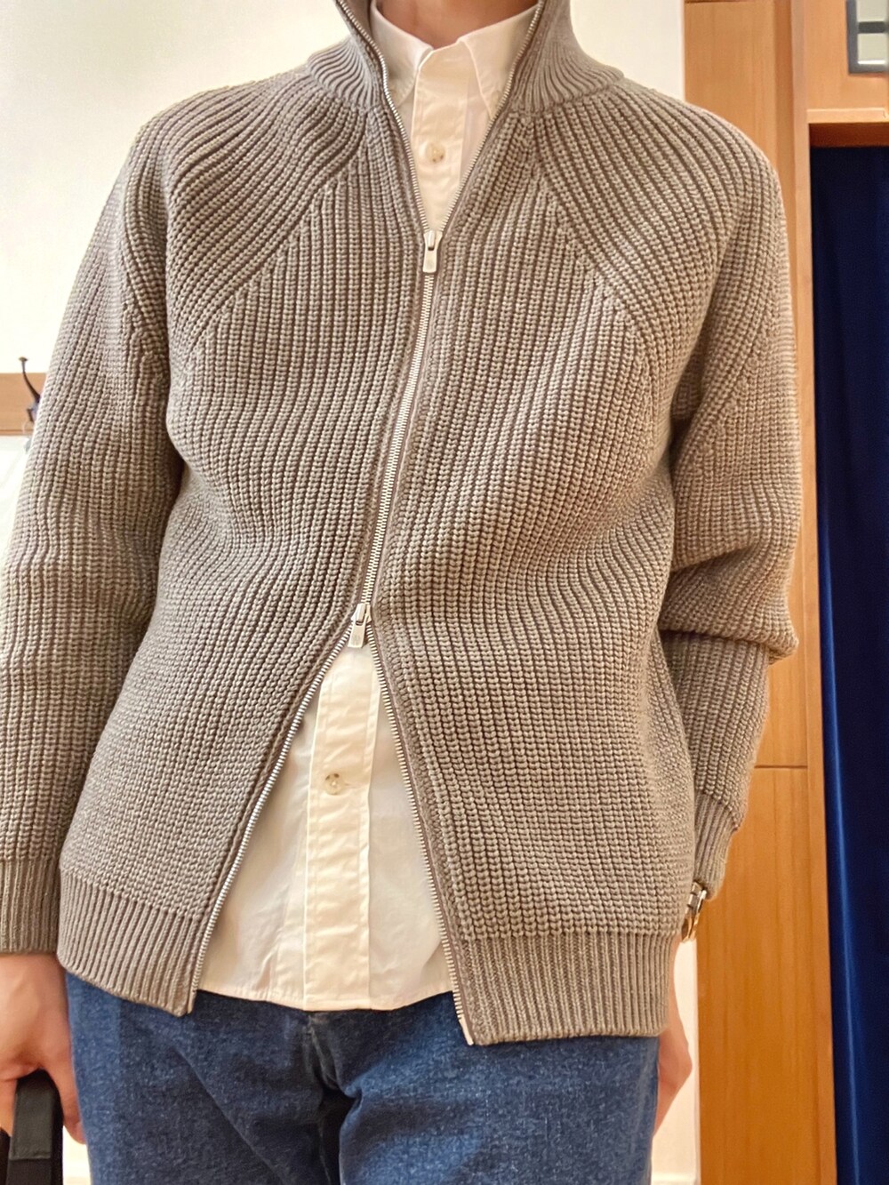 グレー系のニット/セーター、ホワイト系のシャツ/ブラウス、ブルー系のデニムパンツを着用したメンズの秋コーディネートの9枚目の写真