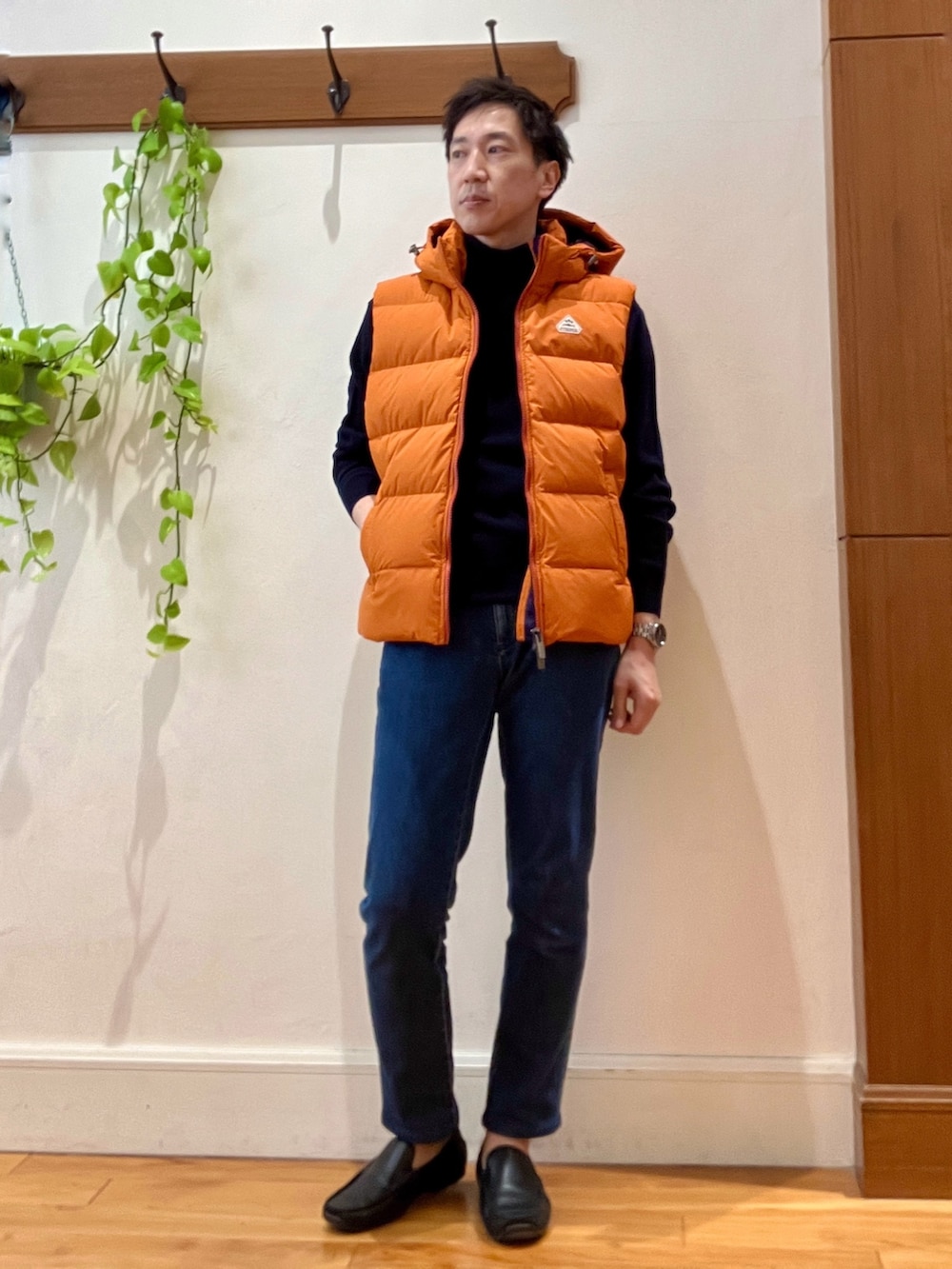 ブルー系のデニムパンツ、ブルー系のニット/セーター、オレンジ系のダウンベストを着用したメンズの冬コーディネートの2枚目の写真