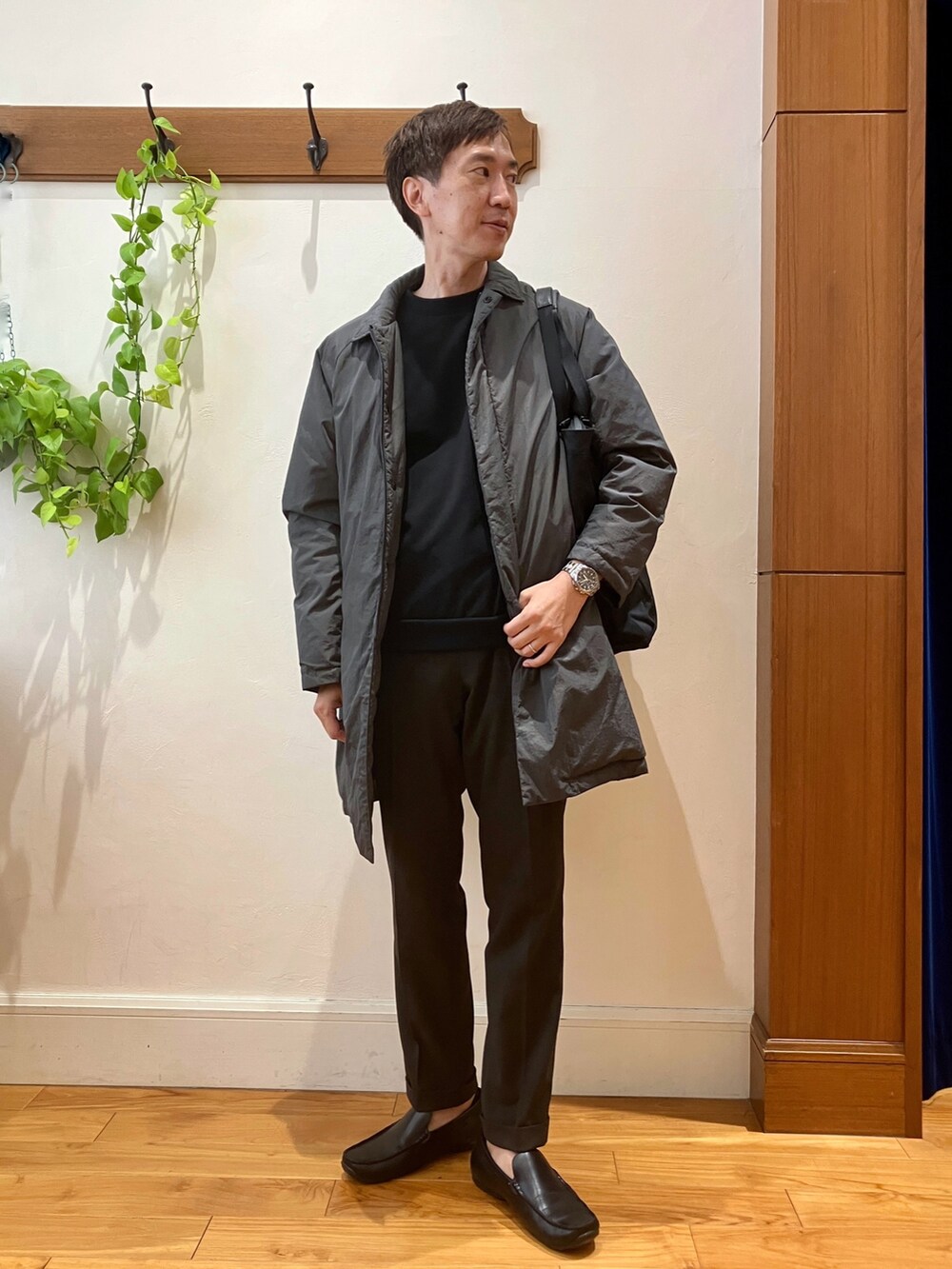 ブラック系のトートバッグ、ブラウン系のスラックス、グレー系のダウンジャケット/コートを着用したメンズの夏コーディネートの2枚目の写真