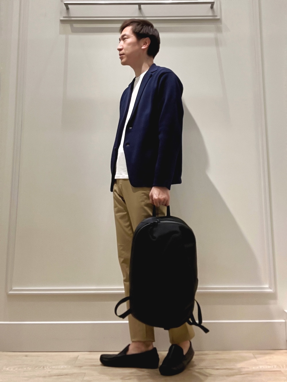 ベージュ系のチノパンツ、ブラック系のバックパック/リュック、ブルー系のカーディガン/ボレロを着用したメンズの冬コーディネートの3枚目の写真