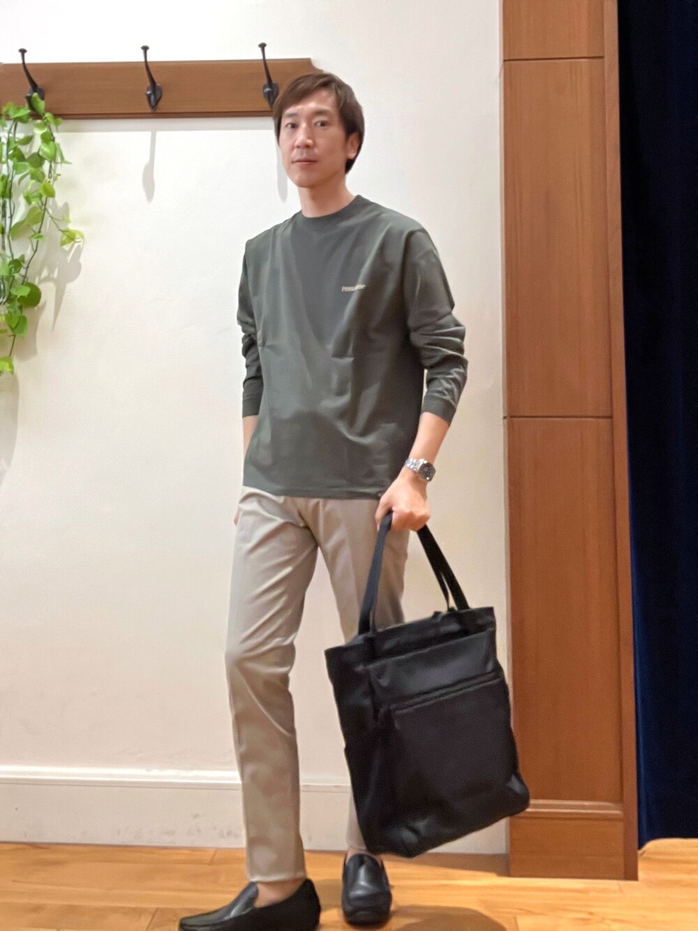 グリーン系のTシャツ/カットソー、グレー系のチノパンツ、ブラック系のトートバッグを着用したメンズの秋コーディネートの4枚目の写真