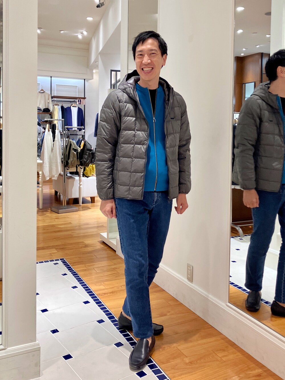 ブルー系のカーディガン/ボレロ、グレー系のダウンジャケット/コート、ブルー系のデニムパンツを着用したメンズの秋コーディネートの2枚目の写真