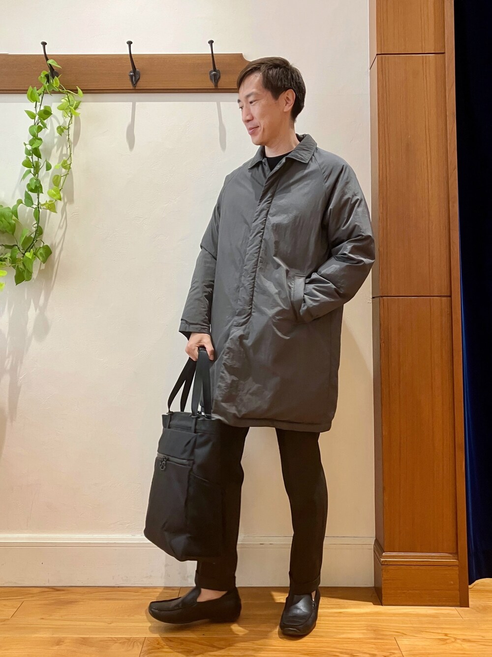 ブラック系のトートバッグ、ブラウン系のスラックス、グレー系のダウンジャケット/コートを着用したメンズの夏コーディネートの3枚目の写真