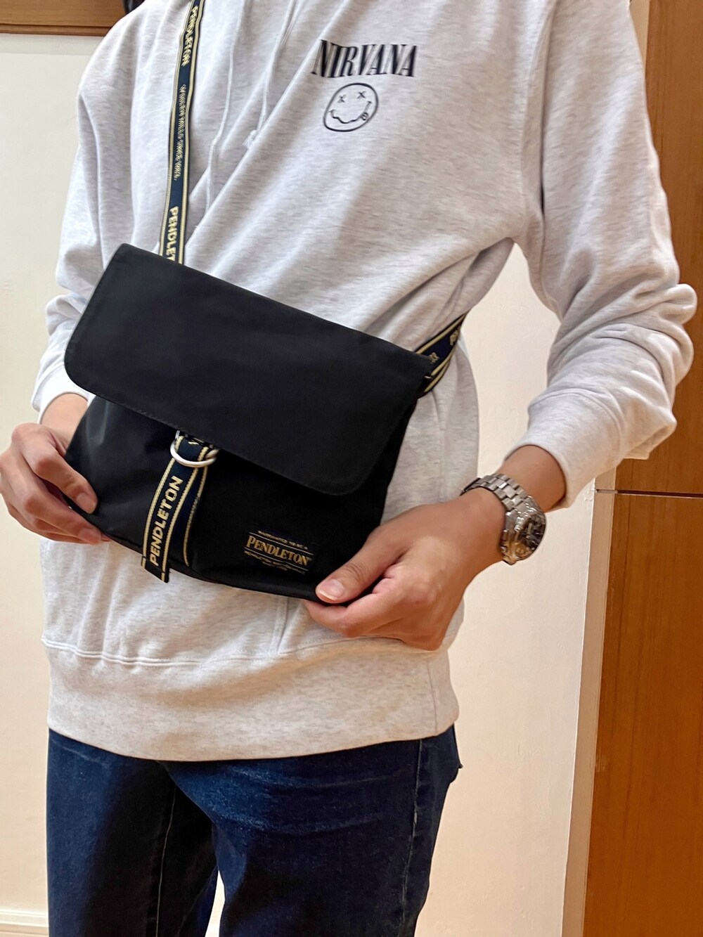 グレー系のパーカー、ブラック系のショルダーバッグ、ブルー系のデニムパンツを着用したメンズの秋コーディネートの4枚目の写真