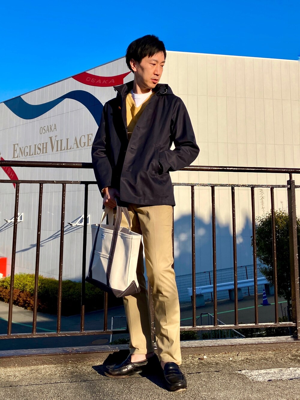 ブルー系のブルゾン、ホワイト系のトートバッグ、ベージュ系のチノパンツを着用したメンズの春コーディネートの7枚目の写真